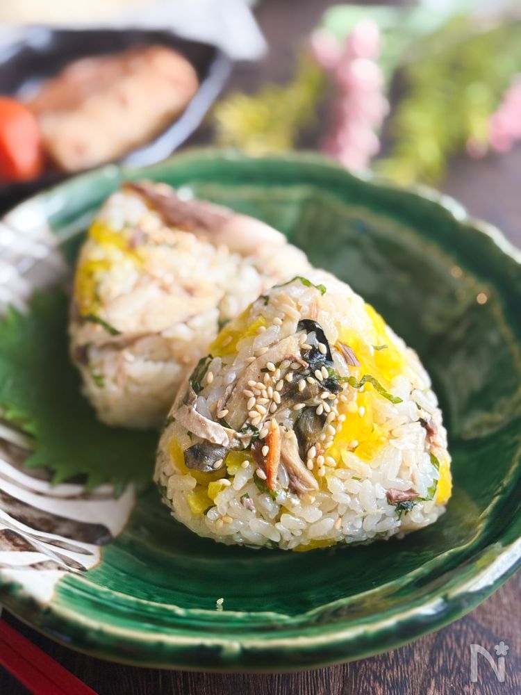 緑色の皿に盛り付けられた塩さばとたくあんのおにぎり