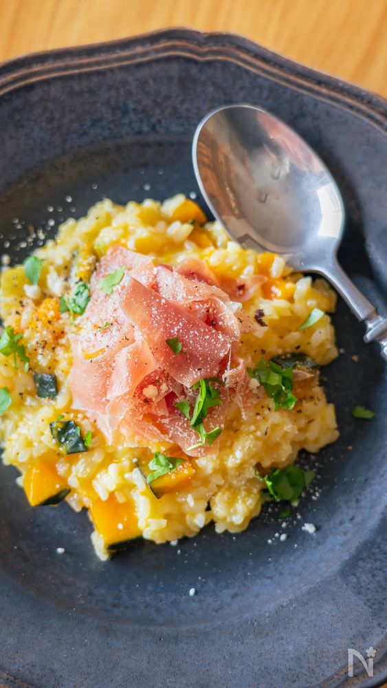 紺色の皿に盛り付けた生ハムとかぼちゃのチーズリゾット