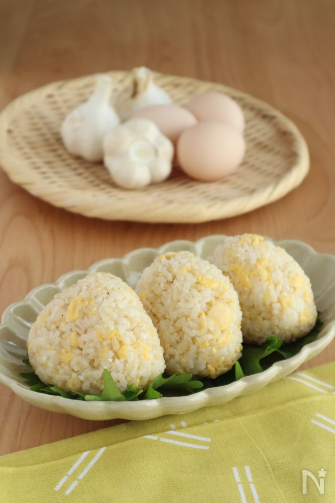 皿に盛り付けられた3個のおにぎりと、かごに置かれたたまごとにんにく