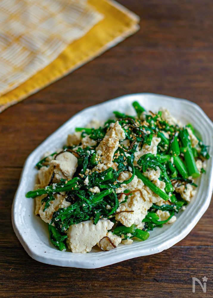 白い楕円型の皿に盛り付けた豆腐と春菊の塩昆布和え