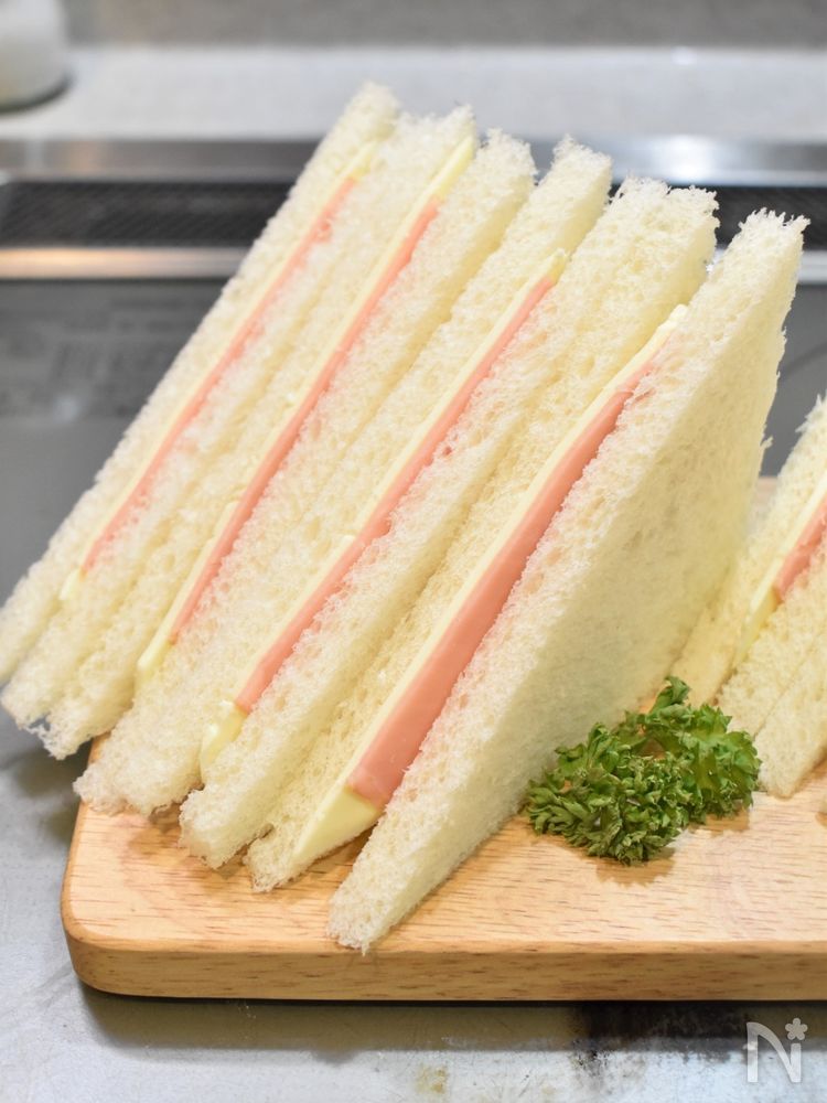 木製のボードにおかれたカットしたスライスチーズハムサンド