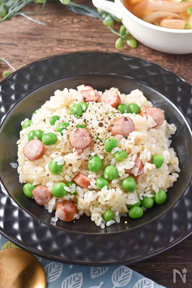 黒い皿に盛りつけられたえんどう豆とウインナーのピラフ