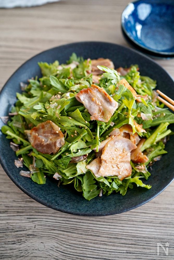 黒色の丸皿に盛られた春菊の豚バラ焼肉サラダ